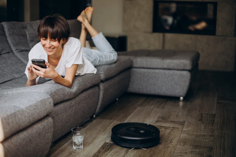 woman-using-phone-while-vacuum-robot-cleaning-thefloor